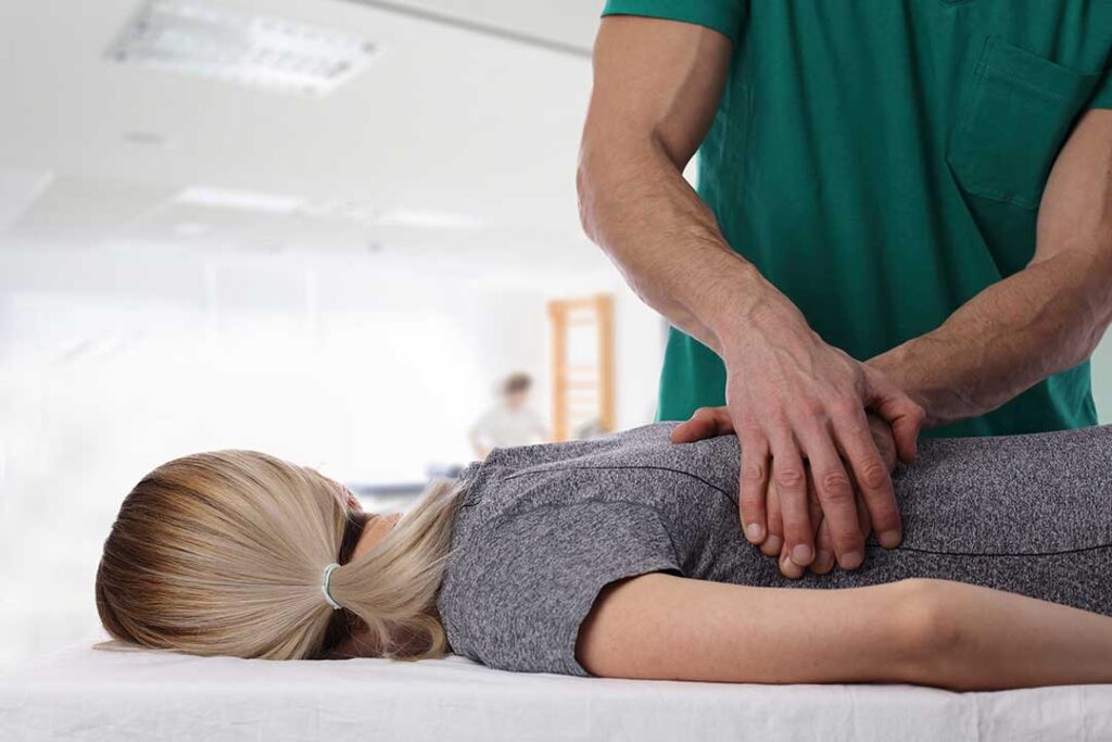 A person sitting on a sofa gently stretching their knee with hands supporting the joint.