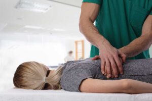 A person sitting on a sofa gently stretching their knee with hands supporting the joint.